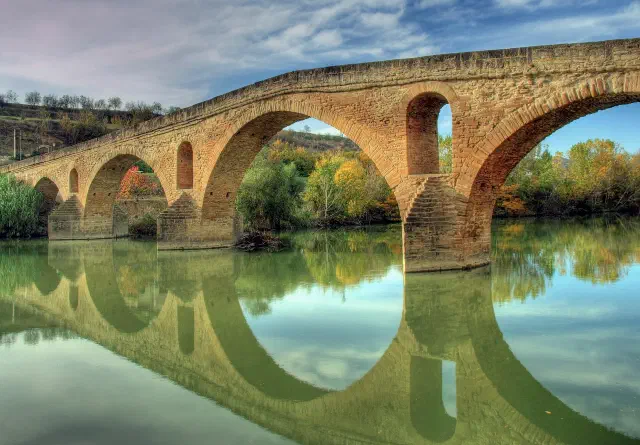 De middeleeuwse stenen brug met zes bogen over de rivier de Arga in Puente la Reina De middeleeuwse stenen brug met zes bogen over de rivier de Arga in Puente la Reina